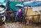 A black guy in rubber boots under an umbrella is pushing a cart in the pouring rain in the rainy season