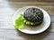 Black hamburger on a white plate on a white wooden background
