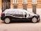 Black hatchback car is covered with transparent plastic wrap and sealed with white tape. Stands parked on street in front of house