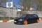 Black hatchback with orange wide wheels tuned by air suspencion parked under different road signs