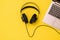 Black headphones connected by wire to the laptop on a yellow background. The concept of workplace organization