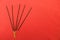 Black incense sticks with yellow tips lie in a fan on the left on a red textile background.