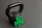 Black iron kettlebell with green shamrock on a black gym floor, holiday fitness