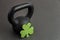 Black iron kettlebell with green shamrock on a black gym floor, holiday fitness