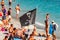 Black Jolly Roger pirate flag on the beach full of sanbathing and swimming tourists in famous Monterosso Al Mare, Cinque Terre,