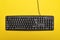 Black keyboard on bright yellow background. Wired computer keyboard. Top view