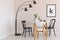 Black lamp above chairs and wooden table with flowers in dining room interior with poster. Real photo