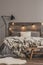 Black lamp and light bulbs on wooden headboard of comfortable bed with grey bedding and warm blanket