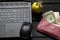 black laptop dollars and an apple lie on a black wooden table in the workplace