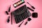 Black leather bag with nail polish, pomade, mascara and eye shadows on pink background composition