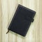 Black leather book on wood background. Blank template of hardcover book