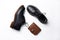 Black leather derby shoes with polyurethane soles and a brown purse with a button on a white background