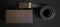 A black leather men\\\'s belt with a gold-tone automatic buckle lies on a dark background next to a gift box. Close-up