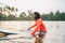 Black long-haired teen man floating on long surfboard, waiting for a wave ready for surfing with palm grove litted sunset rays.