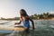 Black long-haired teen man portrait floating on long surfboard in sleeveless telnyashka, waiting for a wave ready for surfing.