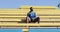 A black male athlete sits in the stands on the stadium in the open air.