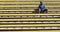 A black male athlete sits on the yellow stairs in a stadium.
