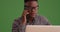 Black male with glasses talks on the phone working on his laptop on green screen