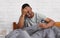 Black Man Having Headache Suffering From Pain Sitting In Bedroom