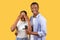 Black man holds proposal ring, woman covers eyes, yellow background, romantic surprise