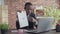 Black man operator in a headset and suit shows the diagrams with pen by video link on laptop and talks while sitting at
