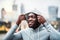 Black man runner with earphones on the bridge in a city, putting hood on head.