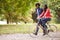 Black man running in a park beside his girlfriend, who is riding a bike, side view