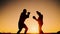 Black man trains to boxing with trainer outdoors in the background of sunset. Bottom view of a silhouette shadow of a