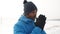 Black man in winter clothes warm gloved hands with his breath and starts jogging, front view. Black athlete man warms