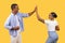 Black man and woman high-fiving, playful interaction, yellow background