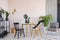 Black mannequin`s leg on wooden chair in elegant dining room interior with round wooden table, metal shelf and retro armchair,