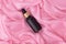 Black matte cosmetic bottle with a dropper on a background of wet crumpled pink silk. Mockup flacon for oil or essence