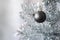 Black matte metallic ball hanging on a silver artificial Christmas tree with copy space. Selective focus. Blurred background