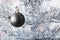 Black matte metallic ball hanging on a silver artificial Christmas tree with copy space. Selective focus. Blurred background