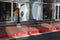 A black metal bench on a red brick sidewalk in front of the glass window of some shops with a red painted curb