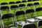 Black metal chairs stand outside in the park in the rain. Empty auditorium, green grass, waterdrops, closeup