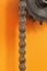Black metal cogwheel and chain on orange background.