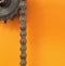 Black metal cogwheel and chain on orange background with empty space.