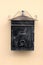 Black metal mailbox in baroque style with faded color mounted on light orange family house wall