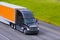 Black modern semi truck orange trailer driving highway line