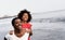 Black mother and daughter running on the beach at sunset time during summer vacation - Focus on mother face