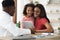 Black mother and daughter visiting pediatrician, holding digital tablet