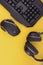 Black mouse, the keyboard, the headphones are isolated on a yellow background, the top view. Flat lay