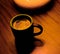 Black mug of coffee on table under lamp, golden