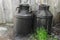 Black and oiled metal canisters in the countryside. Wooden wall
