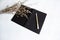 The black opened book with pen put beside dried flowe