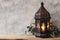 Black ornamental Moroccan, Arabic lantern. Green olive leaves, branches on old wooden table, blurred grunge wall