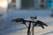 Black pair of modern synthetic gloves stuck on handlebar of folding bike standing in suburban area with blurred background on cold