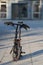 Black pair of modern synthetic gloves stuck on handlebar of folding bike standing in suburban area with blurred background on cold