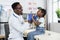 Black pediatrician examining throat of cute child at clinic